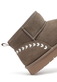 Bruine suede enkellaars met een ronde neus, decoratieve witte stiksels en een gestructureerde rubberen zool. Achterlus voor gemakkelijk aan- en uittrekken.
