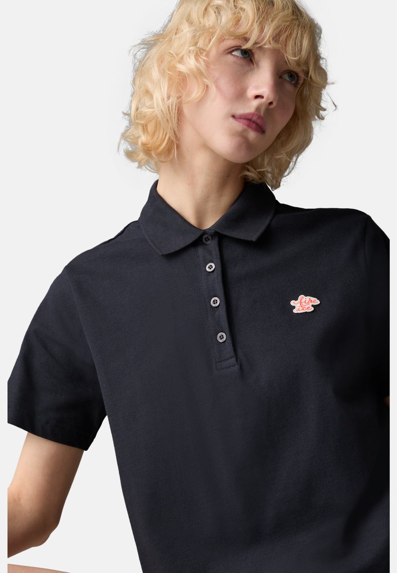 Dunkelblaues Polo-Shirt mit einem klassischen Kragen, fünf Knöpfen und einem kleinen roten Fisch-Logo auf der linken Brust. Hergestellt aus strukturiertem Stoff.