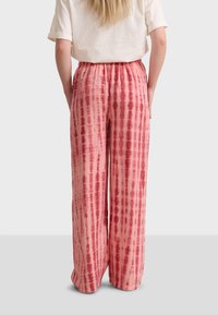 Pink tie-dye wide-leg pants with a soft texture and elastic waistband, featuring vertical lines and variations in color intensity.