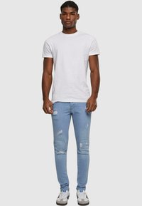 Fehér, kerek nyakú póló, világoskék, szakadt skinny farmerral és fehér sportcipővel, fekete és kék díszítéssel.