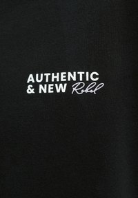 Μαύρο ύφασμα με λευκό και ανοιχτό γκρι κείμενο που γράφει "AUTHENTIC & NEW Rebel" με γράμματα τύπου block και script.