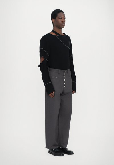 Black long-sleeve top with cut-out shoulders and gray stitching, paired with high-waisted gray trousers featuring large metallic buttons.