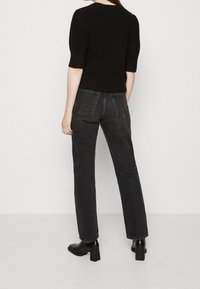 Pull en tricot noir à manches courtes, associé à un jean noir à jambe droite et des bottines à talons épais noires. Texture lisse sur l'ensemble.