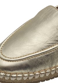 Guldiga läderslip-on-skor med en slät textur, rund tå och sydd jute-detalj runt sulan.