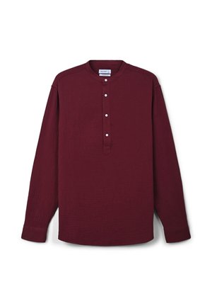 Camicia bordeaux a maniche lunghe con colletto alla mandarino e quattro bottoni bianchi sulla pattina, posata su uno sfondo bianco.