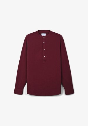 Camicia bordeaux a maniche lunghe con colletto alla mandarino e quattro bottoni bianchi sulla pattina, posata su uno sfondo bianco.