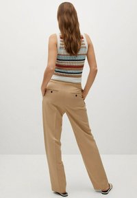 Débardeur tricoté à rayures multicolores ; pantalon large beige avec poches arrière doubles et texture lisse ; modèle vu de dos.