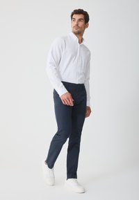 Biele button-up košeľa s dlhými rukávmi, námornícke nohavice a biele tenisky. Nohavice sú úzkeho strihu; košeľa má klasický golier.