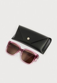 Óculos de sol com lentes cor de rosa e armação quadrada, com lentes castanhas, colocados ao lado de uma caixa preta de couro com fecho de pressão.