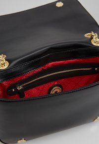 Svart läderhandväska med en slät yta. Insidan har ett livfullt rött foder, en ficka med dragkedja och logodetaljer. Guldfärgade metalldetaljer.