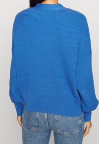 Blå ribbad tröja med hög krage, ballongärmar och avslappnad passform. Bärs med tighta denimjeans.