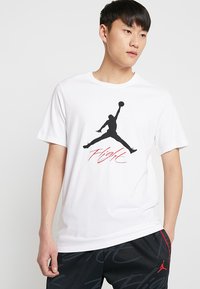 Weißes Baumwoll-T-Shirt mit einer schwarzen Silhouette einer springenden Figur und rotem "Flight"-Text. Design mit Rundhalsausschnitt und kurzen Ärmeln.