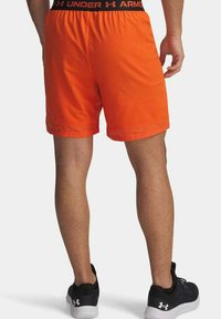 Pantaloni corti sportivi arancioni con un elastico nero in vita, dotati di un dettaglio in rete sull'orlo. Indossati con scarpe sportive nere.