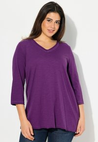 Lila, leichtes V-Ausschnitt-Oberteil mit Dreiviertelärmeln, lockerer Passform und subtiler Textur. Der Saum fällt unter die Hüften.