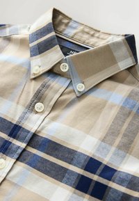 Camisa de cuadros con rayas beige, azul claro y azul marino. Confeccionada en algodón, cuenta con un cuello clásico y cierres de botones.