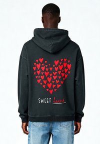 Felpa nera con cappuccio caratterizzata da un grande design a cuore rosso composto da cuori più piccoli, con il testo "SWEET heart" in bianco e rosso sul retro.