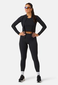 Svart träningsset som innehåller en zip-up jacka, en ribbad crop top och högmidjade leggings. Kompletteras med sportiga solglasögon och sneakers.