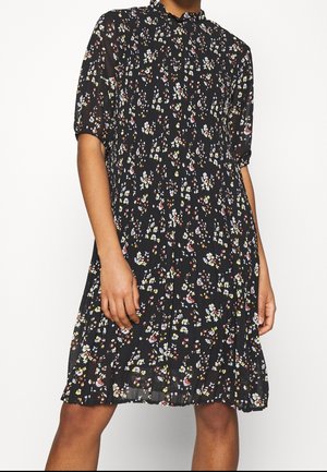 Czarna sukienka o długości do kolan z małym wzorem kwiatowym w białe, żółte i czerwone kolory, krótkie bufiaste rękawy oraz falbaniasty, wysoki kołnierzyk.