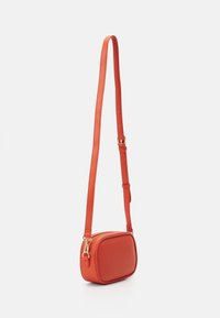 Borsa a tracolla rossa in pelle con forma rettangolare, tracolla regolabile, hardware dorato e finitura texturizzata. Chiusura con zip nella parte superiore.
