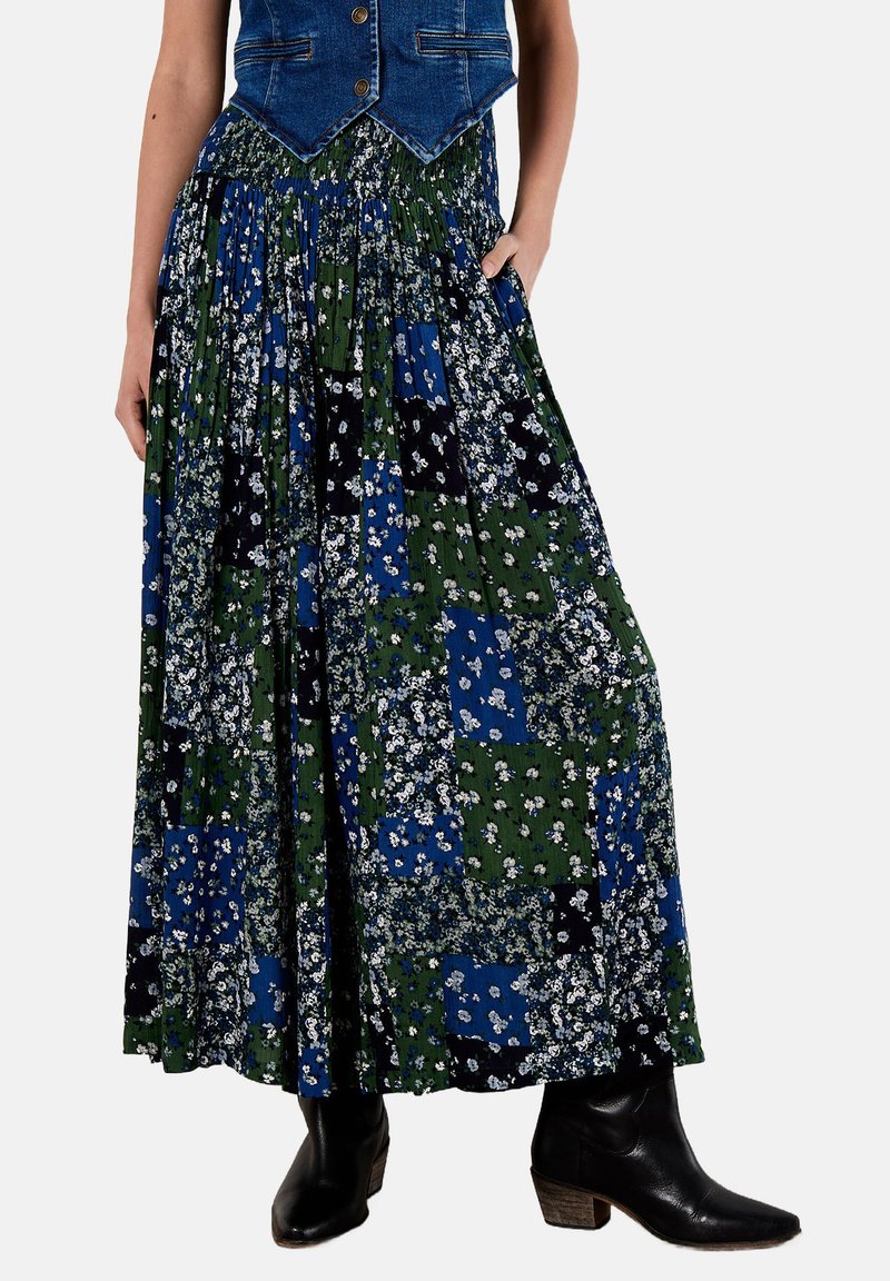 Falda maxi floral con diseño de patchwork en verde, azul y negro, con cintura fruncida y bolsillos laterales. Combina con un chaleco de mezclilla y botas.