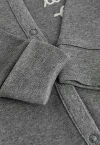 Grauer Cardigan mit glatter Textur, Knopfverschluss und sichtbaren Nähten. Saum ordentlich gefaltet, was ein stimmiges Design zeigt.