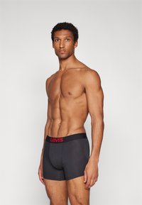 Svart bomullsboxershorts med en röd Levi's-logotyp på midjebandet, som visar en åtsittande form och slät textur, visad på en manlig modell.