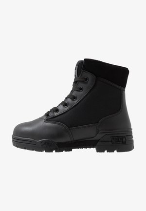 Botte noire cheville en cuir et toile avec un design texturé. Présente des semelles robustes et six œillets pour les lacets. Marquée "Magnum."