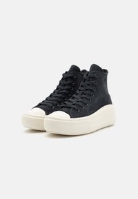 Zapatillas de alta, hechas de gamuza texturizada en azul oscuro, con una puntera de goma blanca y una suela gruesa blanca. Presentan cordones y ojales negros.