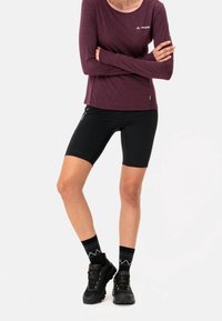 Camicia a maniche lunghe bordeaux con colletto rosa, pantaloncini da ciclismo neri, scarpe nere con dettagli arancioni e calze nere a righe.