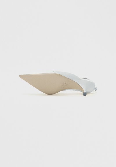 Sapato de salto alto em cetim branco com bico pontiagudo, adornos de joias no salto e na parte superior, sola virada para cima sobre fundo branco liso.