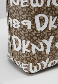Gros plan sur un coin d'un sac DKNY marron à motifs avec du texte blanc de style graffiti comprenant « DKNY », « NEW YORK », et l'année « 1989 ».