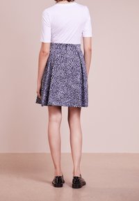 Top bianco a maniche corte abbinato a una gonna blu navy con un motivo testurizzato. Il modello indossa scarpe nere con dettagli borchiati.
