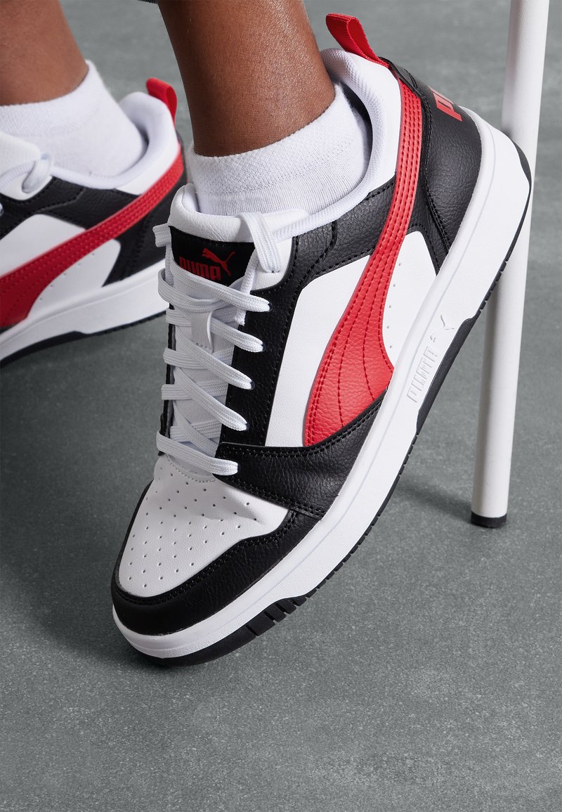Puma-sneakers med en övre del i svart läder och vita samt röda accentfärger, en vit sula och perforerad tå för ventilation. Vita snören.