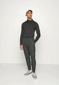 Fekete sportos, hosszú ujjú póló, cipzáras gallérral, fekete, szűkített nadrággal párosítva. A modellen szürke sportcipők és világos színű sapka van.