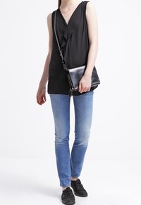 Svart ärmlös topp med volangkrage, matchad med ljusblå skinny jeans och svarta sneakers. Håller en svart crossbody-väska.