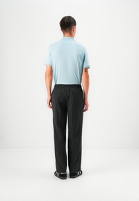 Camisa polo de color azul claro con mangas cortas, combinada con pantalones oscuros de cintura elástica. El modelo muestra la vista trasera, de pie sobre un fondo liso.