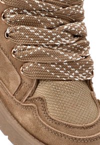Botín marrón hasta el tobillo con tejido trenzado en tono marrón claro y acentos blancos, que presenta cordones trenzados, ojales metálicos y detalles de ante texturizado.