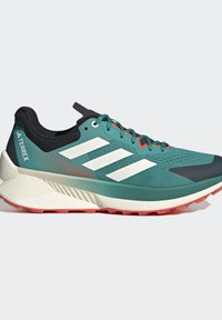 Türkis-schwarzer Adidas Terrex Trailrunning-Schuh mit weißen Streifen, dicker weißer Sohle und orangefarbenem Profil auf einfarbigem Hintergrund.
