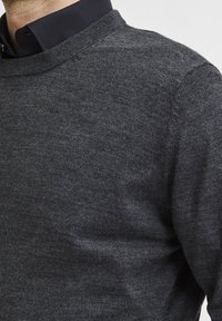 Man wearing dark grey knit sweater over black collared shirt, showing upper chest and shoulder details.