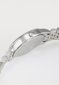 Montre en acier inoxydable argenté avec un boîtier rond, une lunette texturée et un bracelet à maillons. Présente une couronne avec un logo.