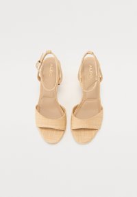 Sandales tissées beiges avec une large bride avant, une bride cheville avec une boucle et une finition douce et texturée sur une semelle plate.