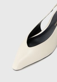 Kreemi värvi teravtoe slingback kingad, millel on sügav lõige ja must sisemus, sile naha pealispind ning minimaalne õmbluste detail.