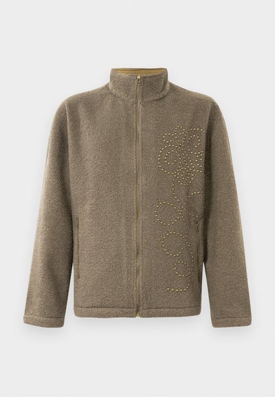 Pruun fliisjakk, millel on kõrge kaelus, lukuga sulgemine ja kaunistavad kuldsed nupud keerduvas mustris ühel küljel.