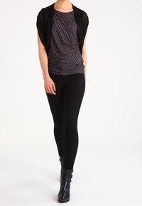 Svart draperad kofta över en mönstrad marinblå topp, ihop med svarta skinny jeans och svarta ankelstövlar. Enkel och strömlinjeformad design.