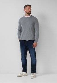 Grijze trui met lange mouwen, ronde halslijn, gecombineerd met donkerblauwe jeans en witte sneakers met beige accenten. Eenvoudig, casual ontwerp.