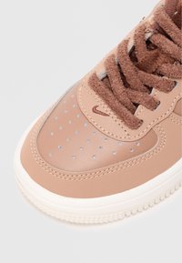 Barna bőr sneaker, texturált velúr nyelvvel, perforált orr résszel és kontrasztos világoskék részletekkel. Lapos barna fűzőkkel és fehér talppal rendelkezik.