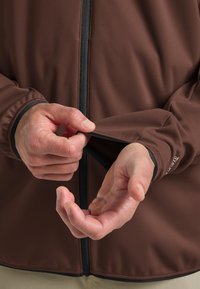 Giacca marrone con zip in tessuto texture. Presenta polsini elasticizzati, zip a vista e una mano che regola la manica. Design semplice e funzionale.