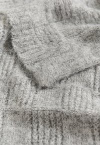 Tissu tricoté gris avec une surface texturée et duveteuse. Présente un motif de côtes verticales et une épaisseur de fil variable dans un matériau doux et chaud.