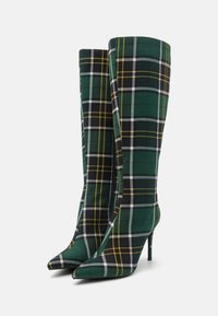 Bottes à carreaux vert et noir jusqu'au genou avec des bouts pointus et des talons aiguilles ; le tissu présente des motifs à carreaux jaunes et blancs.