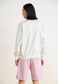 Felpa grigia chiaro con maniche lunghe, polsini e orlo a coste; abbinata a pantaloni corti rosa chiaro. Etichetta evidente sulla tasca dei pantaloni.